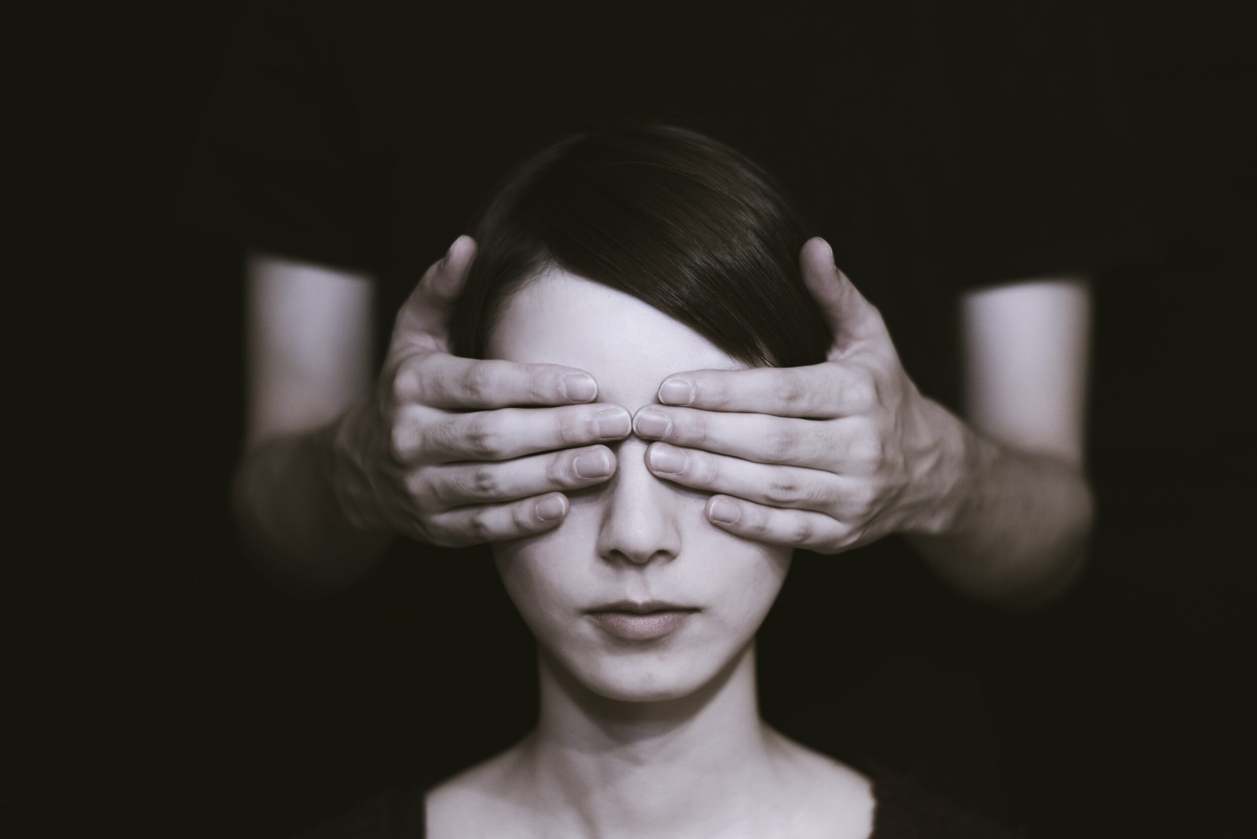 Videoiden kuvailutulkkaus -artikkelin kuvassa tummatukkaisen naisen silmiä peittävät mustapaitaisen miehen kädet takaapäin.