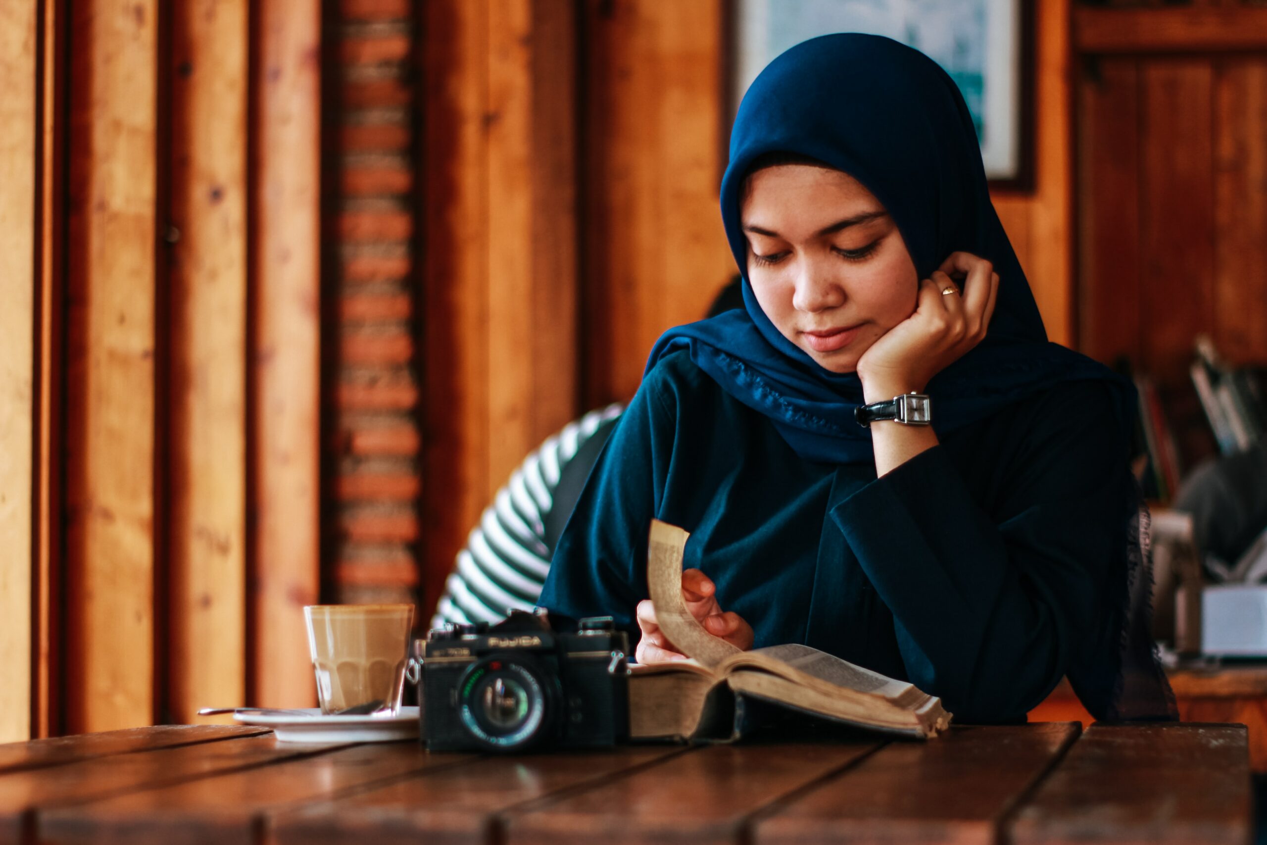 Selkokieli on osa kielellistä saavutettavuutta -artikkelin kuva, jossa musliminainen istuu pöydän ääressä nojaten käteensä ja lukien avonaista kirjaa pöydällä.