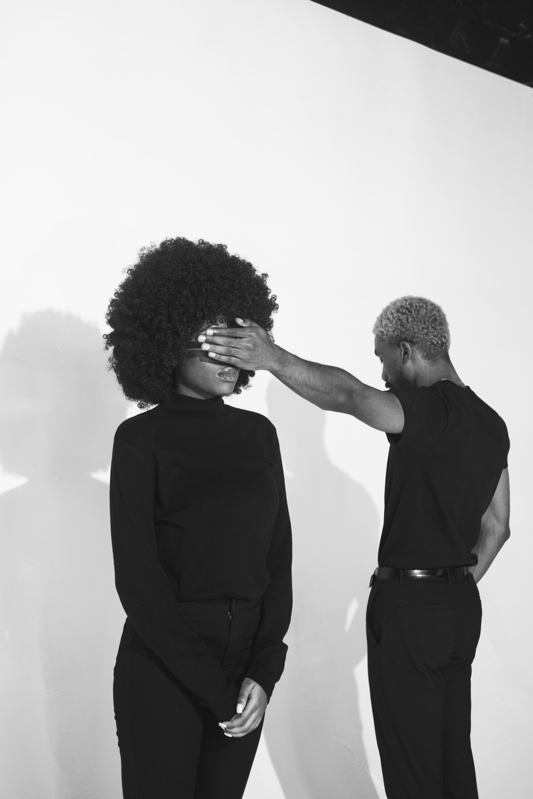 Kuvailutulkkaus pähkinänkuoressa artikkelin mustavalkoinen kuva, jossa mies ja nainen seisovat valkoista seinää vasten ja mies pitää kättään afrotukkaisen naisen silmillä.